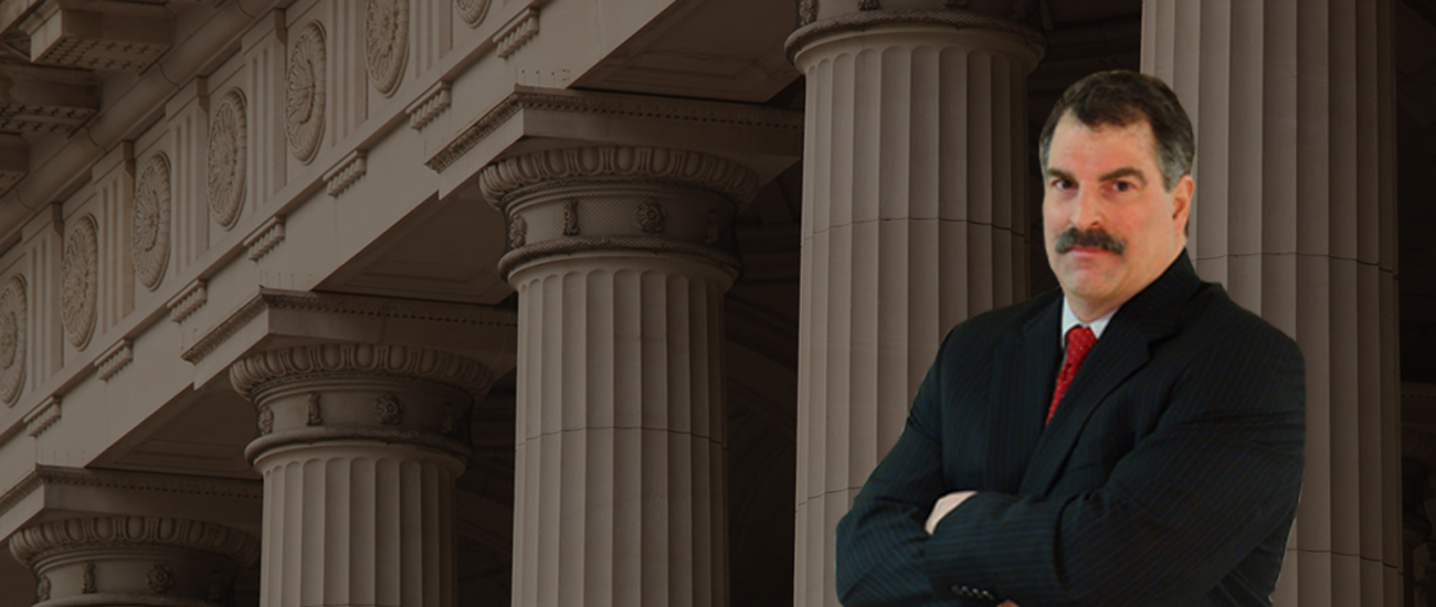 David C. Ricci standing confidently with his arms crossed in front of a courthouse with prominent columns.